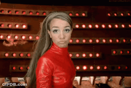 A Woman In A Red Leather Outfit Is Standing In Front Of A Wall Of Red Lights GIF