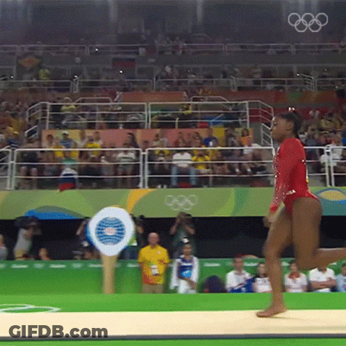 A Woman In A Red Leotard Is Doing A Routine In Front Of A Crowd That Is Watching The Olympics GIF