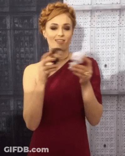 A Woman In A Red One Shoulder Dress Is Holding A Card GIF