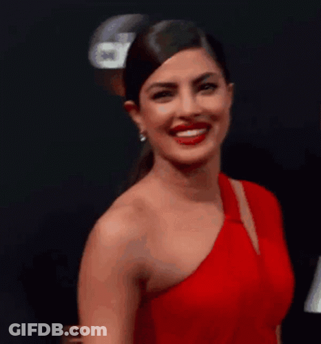 A Woman In A Red One Shoulder Dress Is Smiling And Looking At The Camera . GIF