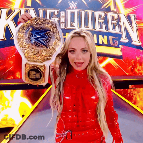 A Woman In A Red Outfit Is Holding A Wrestling Championship Belt In Front Of A King Queen Sign GIF