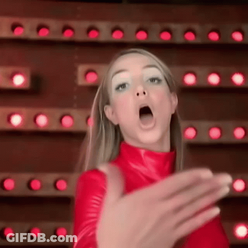A Woman In A Red Outfit Is Making A Funny Face In Front Of A Wall Of Lights . GIF