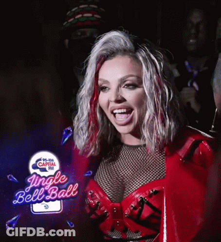 A Woman In A Red Outfit Is Smiling In Front Of A Jingle Bell Ball Sign GIF