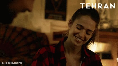 A Woman In A Red Plaid Shirt Is Smiling And Tehran Is Written Above Her GIF