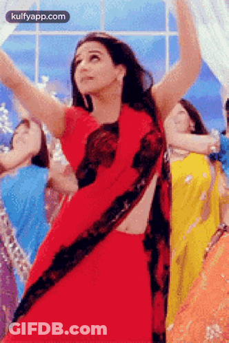 A Woman In A Red Saree Is Dancing In Front Of A Group Of Women In Different Colored Dresses . GIF