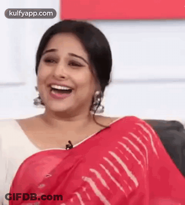 A Woman In A Red Saree Is Laughing While Sitting On A Chair . GIF