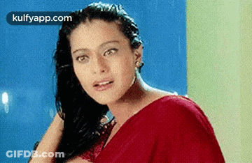 A Woman In A Red Saree Is Looking At The Camera While Holding Her Hair . GIF