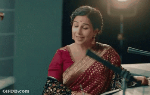 A Woman In A Red Saree Is Sitting In Front Of A Microphone And Says It Would Be My Absolute Pleasure . GIF
