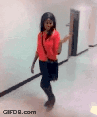 A Woman In A Red Shirt And Black Skirt Is Walking Down A Hallway GIF