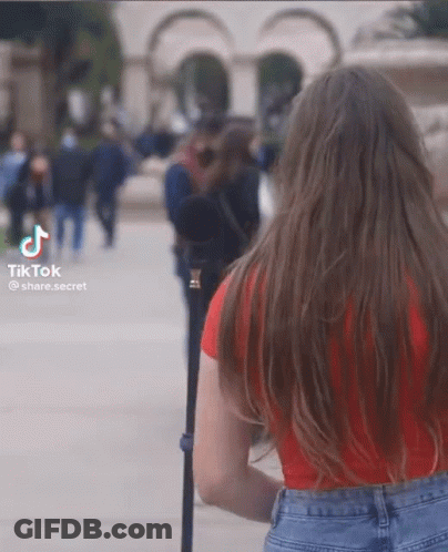 A Woman In A Red Shirt And Blue Jeans Is Walking Down The Street GIF