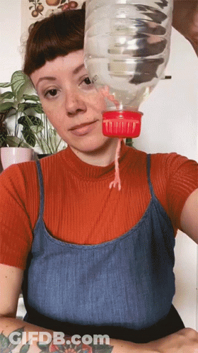 A Woman In A Red Shirt And Blue Tank Top Is Holding A Plastic Bottle With A Measuring Cup On It GIF