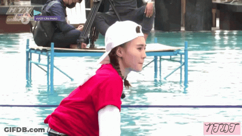 A Woman In A Red Shirt And White Hat Is Kneeling In A Pool With A Watermark That Says Neqt GIF