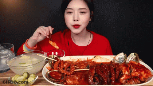 A Woman In A Red Shirt Is Eating A Large Plate Of Food With Chopsticks GIF