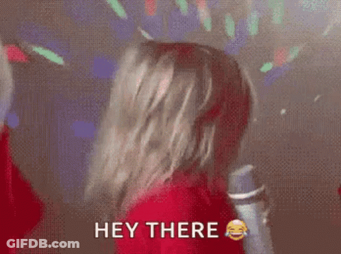 A Woman In A Red Shirt Is Holding A Microphone And Says Hey There . GIF