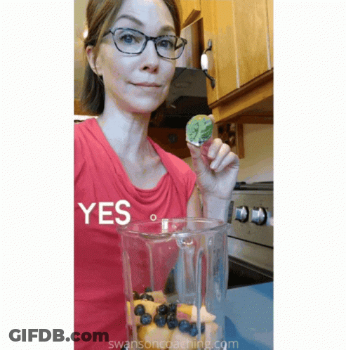 A Woman In A Red Shirt Is Holding A Piece Of Fruit In Front Of A Blender That Says Yes GIF
