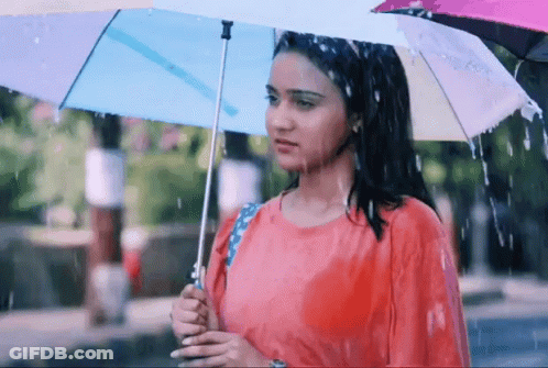 A Woman In A Red Shirt Is Holding An Umbrella While Standing In The Rain GIF