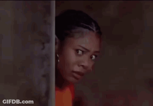 A Woman In A Red Shirt Is Leaning Against A Wall And Looking At The Camera . GIF