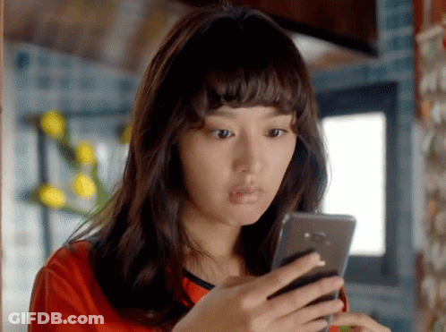 A Woman In A Red Shirt Is Looking At A Cell Phone GIF