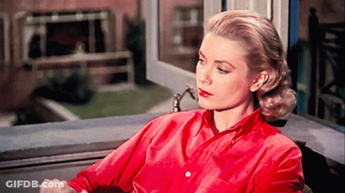 A Woman In A Red Shirt Is Looking Out Of A Window GIF