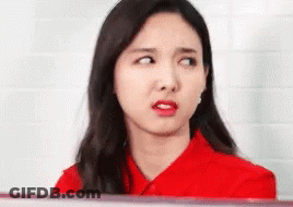 A Woman In A Red Shirt Is Making A Funny Face And Looking At The Camera . GIF