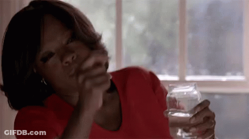 A Woman In A Red Shirt Is Sitting At A Table Holding A Glass Of Water In Her Hand . GIF