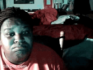 A Woman In A Red Shirt Is Sitting In Front Of A Bed With A Red Blanket On It GIF