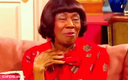 A Woman In A Red Shirt Is Sitting On A Pink Couch Making A Funny Face GIF
