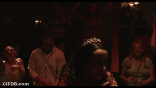 A Woman In A Red Shirt Is Smiling In A Crowd GIF