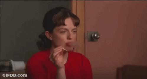 A Woman In A Red Shirt Is Smoking A Cigarette While Sitting In Front Of A Door . GIF