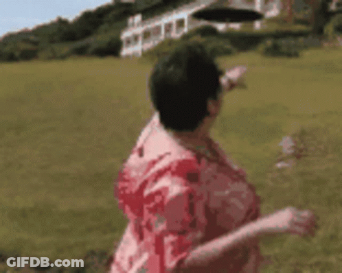 A Woman In A Red Shirt Is Standing In A Field Pointing At Something . GIF