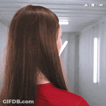 A Woman In A Red Shirt Is Standing In A Hallway With An Adidas Logo On The Bottom GIF