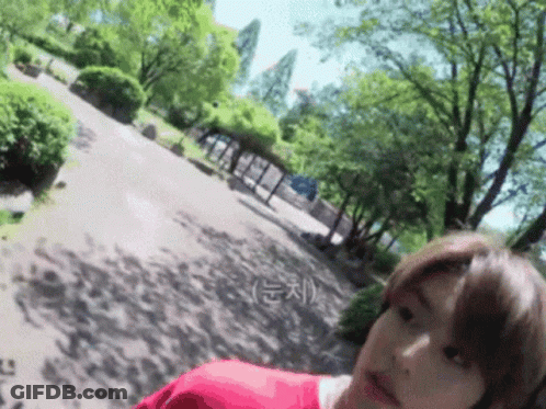 A Woman In A Red Shirt Is Standing In A Park GIF