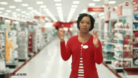 A Woman In A Red Shirt Is Standing In An Aisle Of A Store GIF