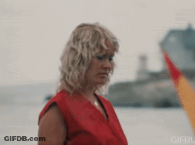 A Woman In A Red Shirt Is Standing In Front Of A Body Of Water GIF