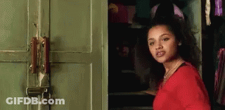 A Woman In A Red Shirt Is Standing In Front Of A Green Door With A Padlock On It . GIF