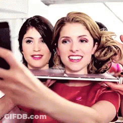 A Woman In A Red Shirt Is Taking A Selfie With Another Woman Behind Her . GIF