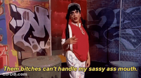 A Woman In A Red Shirt Says " Them Bitches Can 'T Handle My Sassy Ass Mouth " While Standing In Front Of Graffiti GIF