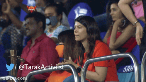 A Woman In A Red Shirt Sits In A Stadium With A Twitter / @Tarakactivist Written Below Her GIF