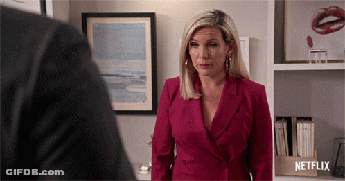 A Woman In A Red Suit Is Standing In Front Of A Netflix Box GIF