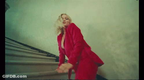 A Woman In A Red Suit Is Walking Down The Stairs GIF