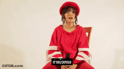 A Woman In A Red Sweater And Hat Is Sitting In A Chair Holding A Microphone . GIF