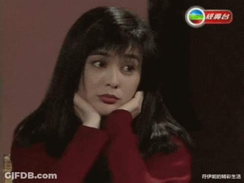 A Woman In A Red Sweater Has Her Hands On Her Face In Front Of A Tv Screen With Chinese Writing GIF