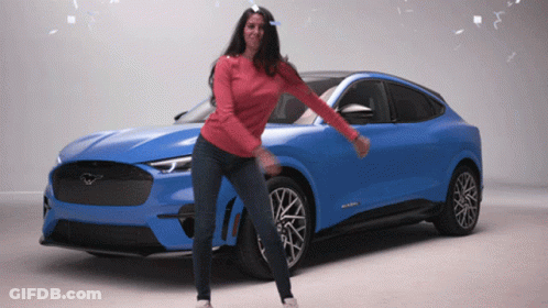 A Woman In A Red Sweater Is Dancing In Front Of A Blue Mustang GIF