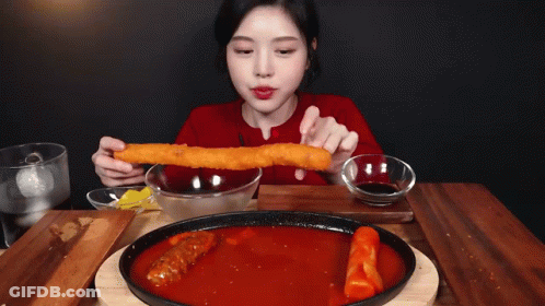 A Woman In A Red Sweater Is Eating A Large Piece Of Food GIF