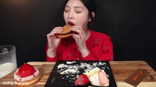 A Woman In A Red Sweater Is Eating A Sandwich With Strawberries On It GIF