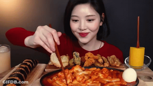 A Woman In A Red Sweater Is Eating Food With Chopsticks .. GIF