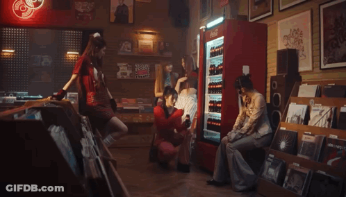 A Woman In A Red Sweater Is Holding A Bottle Of Coca Cola In Front Of A Refrigerator . GIF