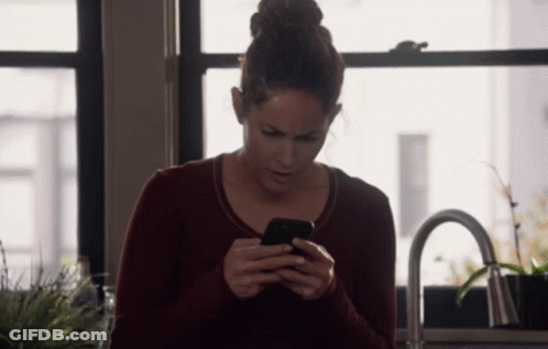 A Woman In A Red Sweater Is Looking At Her Phone GIF