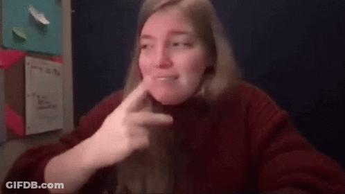A Woman In A Red Sweater Is Making A Funny Face While Sitting At A Table . GIF