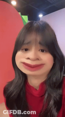 A Woman In A Red Sweater Is Making A Funny Face With Her Mouth Wide Open . GIF